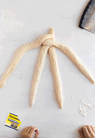 Two hands braiding strips of dough